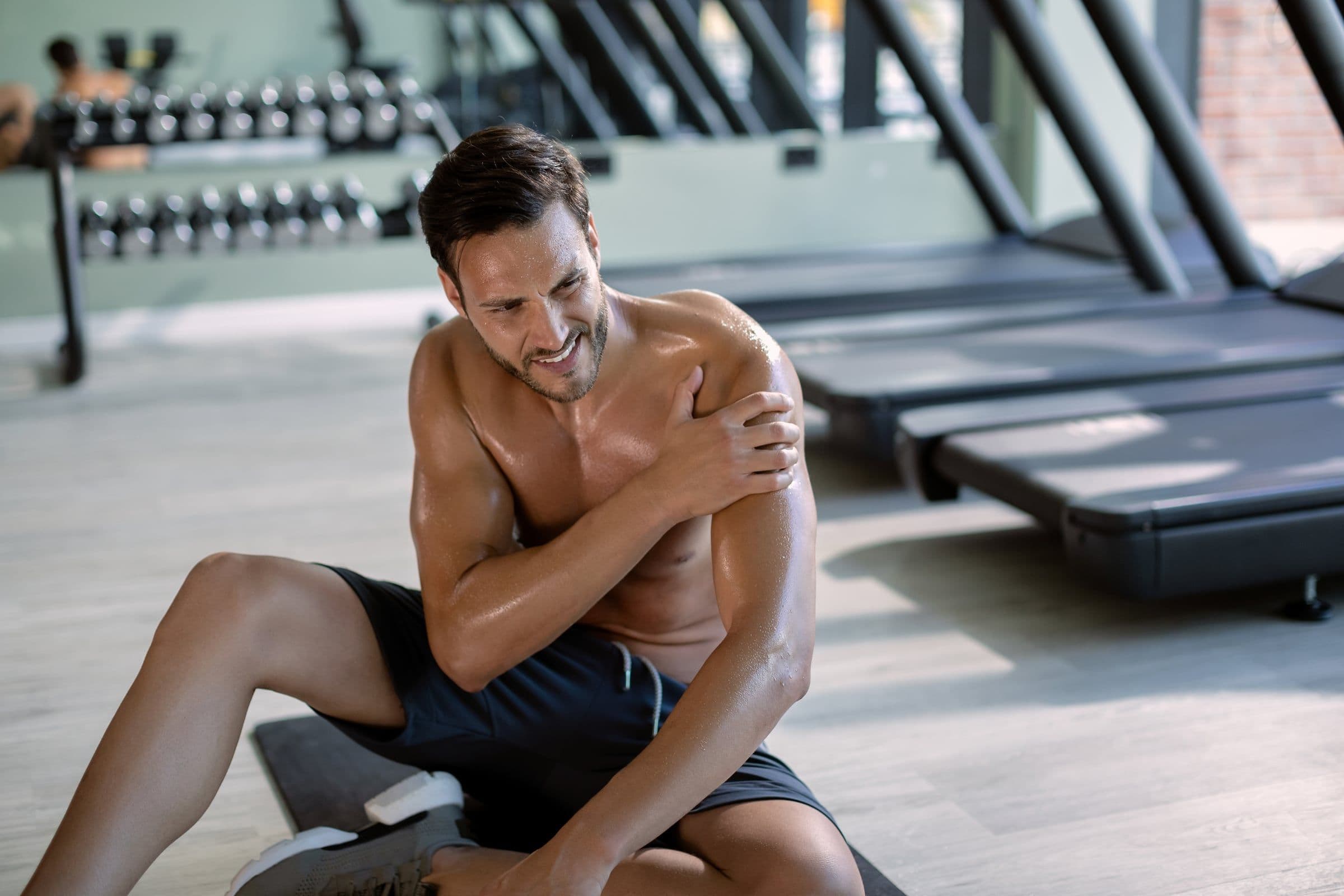 Fiatal sportoló tartja a vállát fájdalmában egy edzőteremben végzett sportedzés után